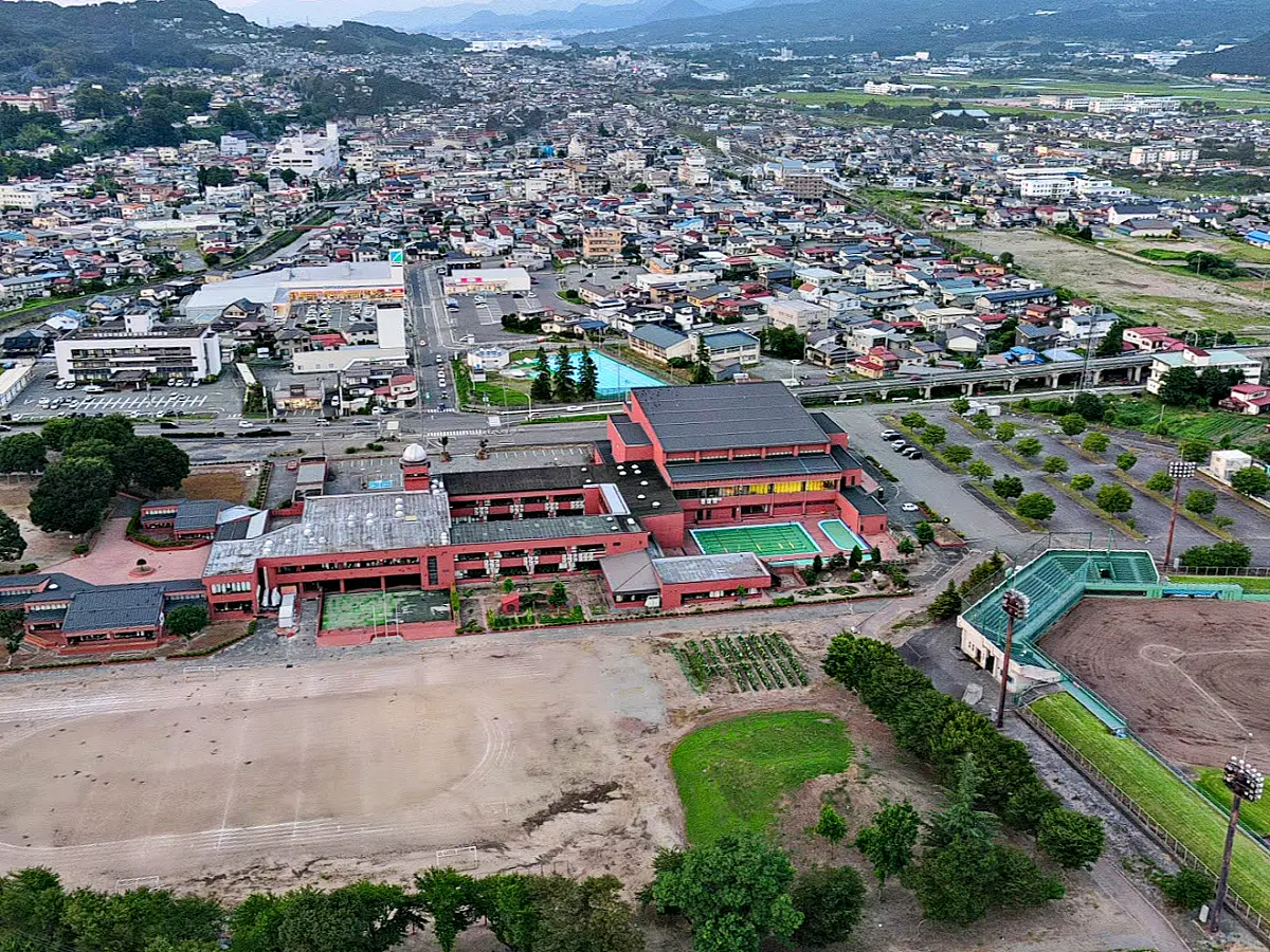 写真中央の赤レンガの建物が南小、その奥に旧市民プール = 2022年7月29日 上山市体育文化センター上空
